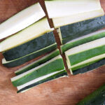 Raw slices of zucchini sitting on a wood cutting board.