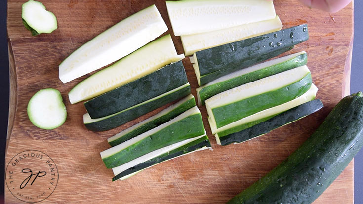 Raw slices of zucchini sitting on a wood cutting board.