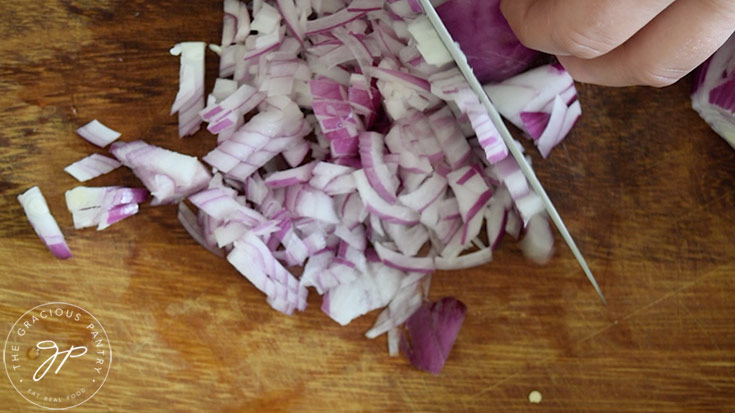 A purple onion being sliced on a wood cutting board.