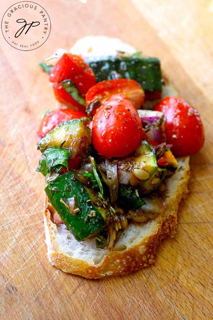 Grilled Zucchini Salad spooned over a thin slice of bread, sitting on a wood cutting board.