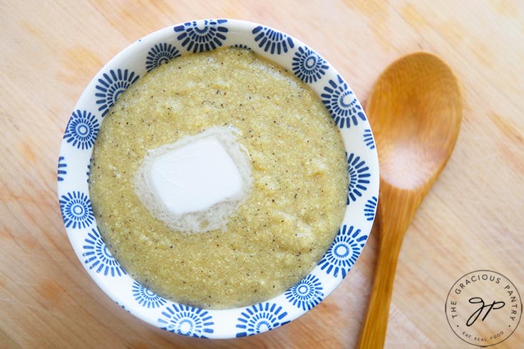 Millet grits in a small bowl with a wooden spoon sitting to the right on a wooden surface.