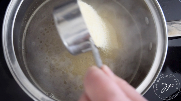 Pouring grits into a pot of boiling water.