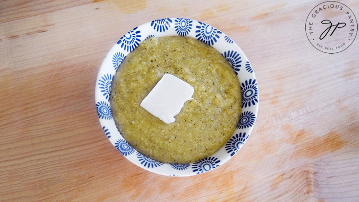 Millet grits in a small bowl with a pat of butter on top.