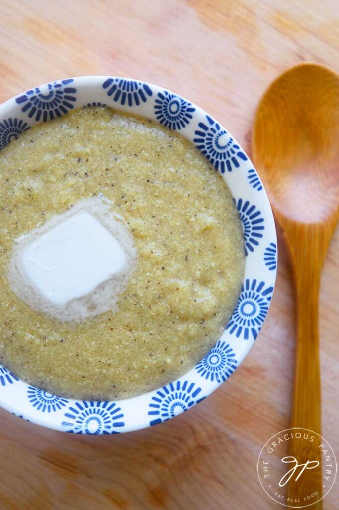 An overhead view of a small, decorative bowl filled with millet grits with a pat of butter on top.