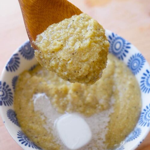 A spoonful of millet grits being held over a serving bowl.