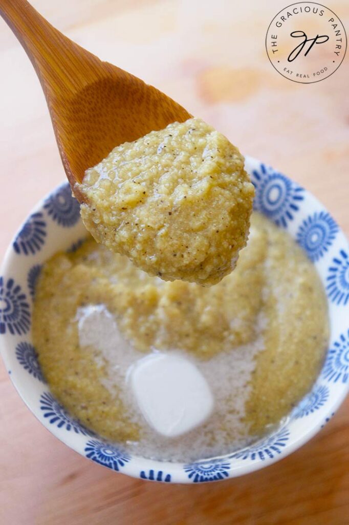 A spoonful of millet grits being held over a serving bowl.