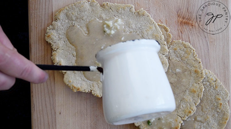 Pouring melted garlic butter over oat flour flatbread.