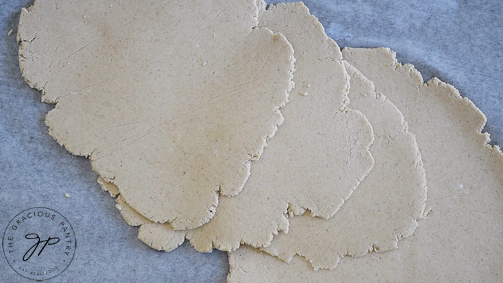 Several just-rolled pieces of raw flatbread dough laying on a piece of parchment paper.