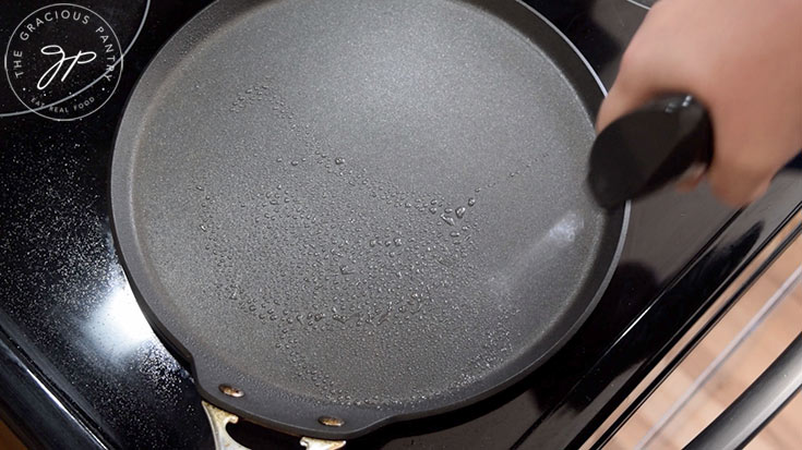 An oil sprayer spraying a skillet on a stove.