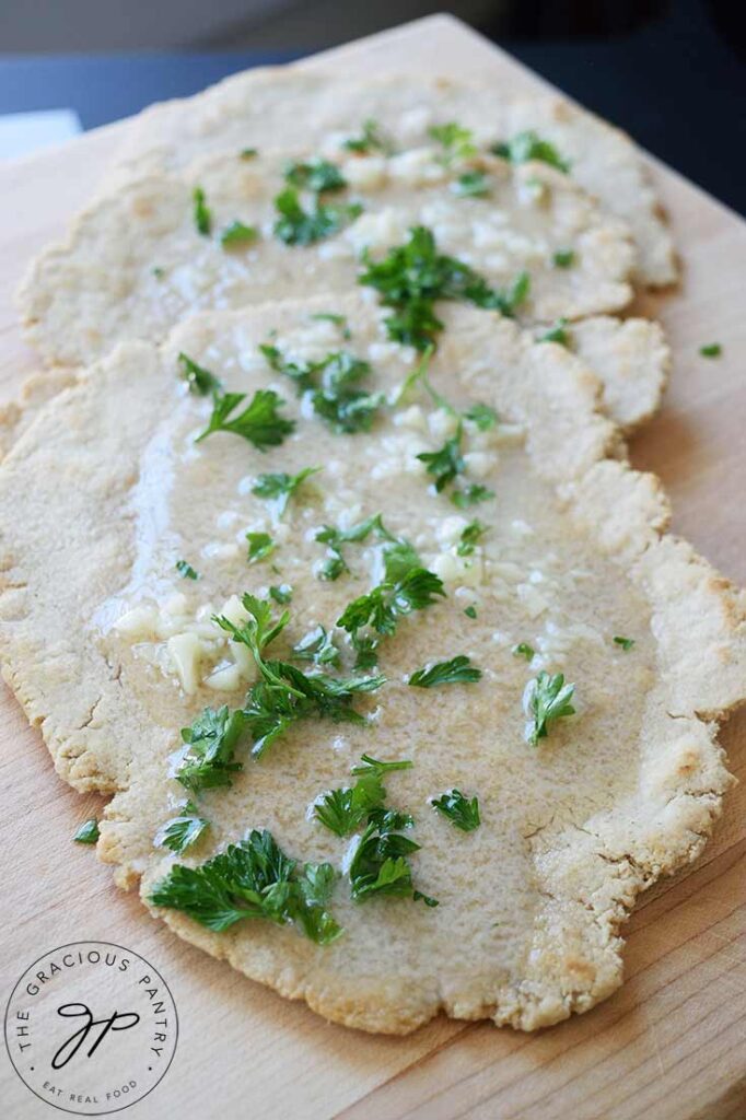 Three oat flour flatbreads laying on a cutting board, garnished with melted garlic butter and fresh parsley.