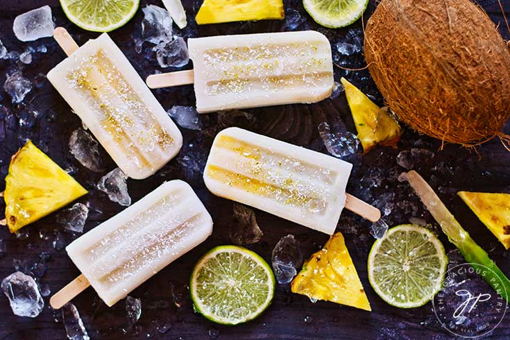 Finished Pineapple Popsicles on a dark background with lime slices and pineapple wedges.
