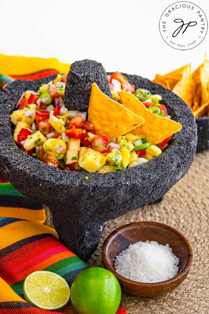 Pineapple salsa in a stone salsa bowl with two corn chips inserted into the salsa.