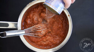 Adding water to refried beans and salsa in a pot.