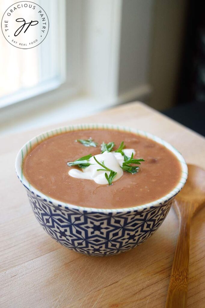 A front view of a bowl of refried bean soup garnished with plain yogurt and fresh cilantro.