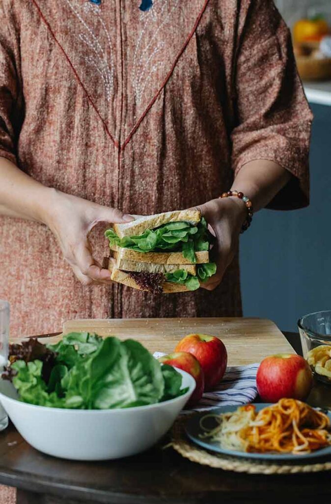 A woman holds up a stack of two sandwiches over a cutting board.