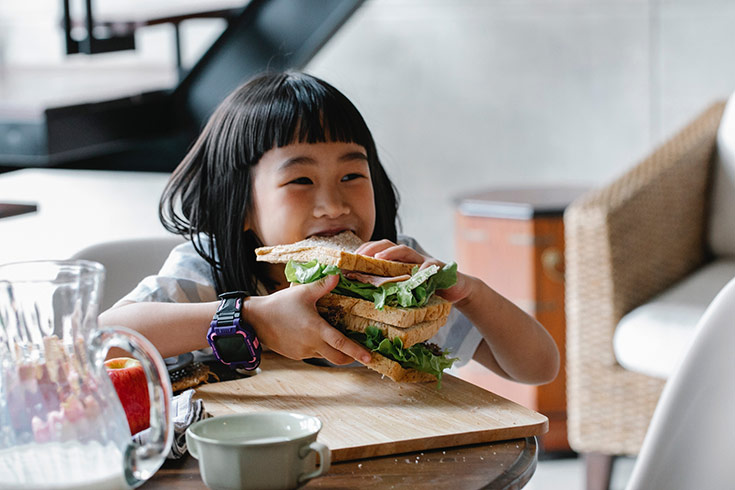 A little girl holding a stack of sandwiches holds up the stack to take a bite.