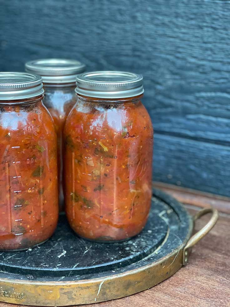 Three canning jars sit on a counter, filled with salsa.