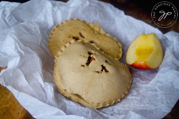 Two just-baked Apple Hand Pies sitting on parchment paper.