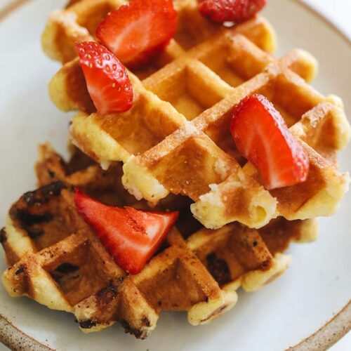 Two Belgian Waffles stacked on a plate and topped with chopped strawberries.