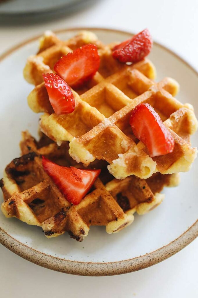 Two Belgian Waffles stacked on a plate and topped with chopped strawberries.