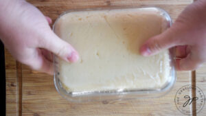 Turning firm Chickpea Tofu from a glass dish out onto a wood cutting board.