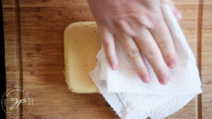 Patting excess oil off the bottom of a loaf of Chickpea Tofu.