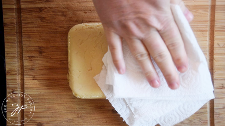 Patting excess oil off the bottom of a loaf of Chickpea Tofu.