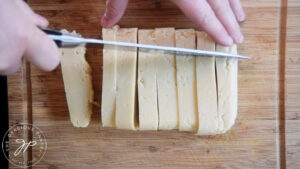 Slicing Chickpea Tofu into cubes on a wood cutting board.