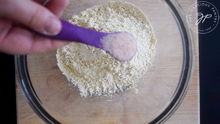 Salt being added to chickpea flour in a glass mixing bowl.