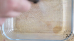 A glass dish being sprayed with oil from an oil sprayer.