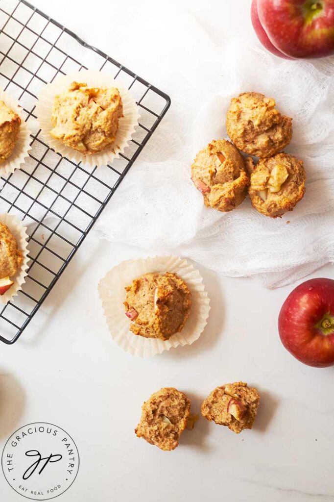 An overhead view looking down on some cinnamon apple muffins and some apples on a white surface.