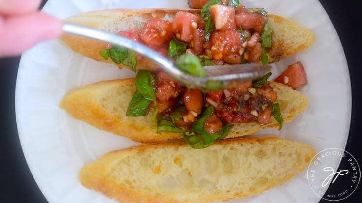 Spooning tomato mixture over toasted bread slices.