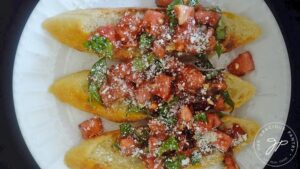 Three Classic Bruschetta on a white plate, garnished with grated parmesan cheese.