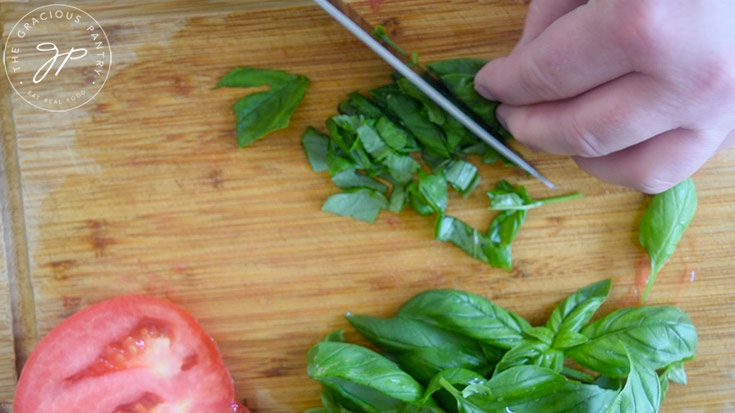 Fresh basil being chopped on a wood cutting board for classic bruschetta.