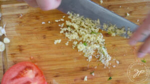 Fresh garlic being minced on a wood cutting board.