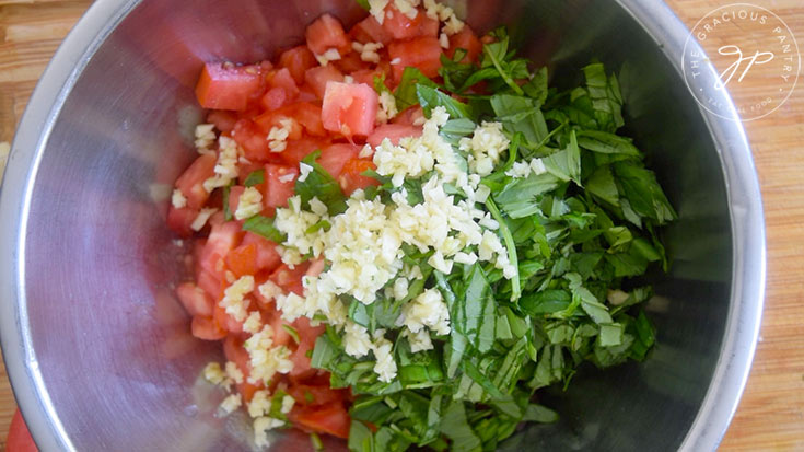 A mixing bowl holding chopped tomatoes, basil and garlic.