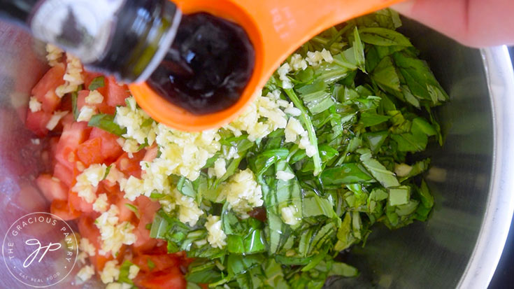 Adding balsamic vinegar to a mixing bowl of tomatoes, basil and garlic.