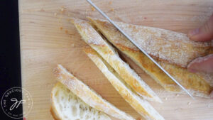 Slicing a baguette on a wooden cutting board.