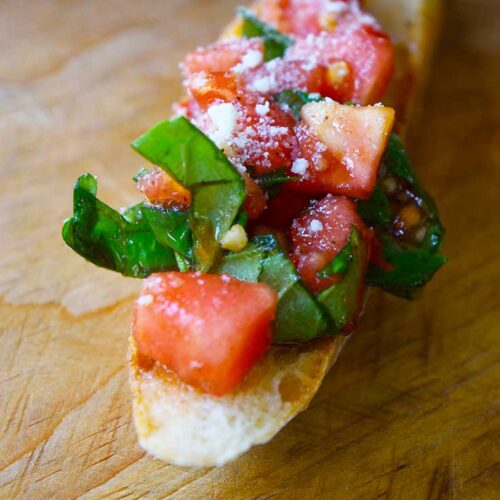 A front view of a single, Classic Bruschetta sitting on a wooden surface.