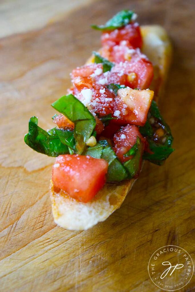 A front view of a single, Classic Bruschetta sitting on a wooden surface.