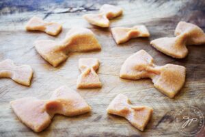 Cooked Complete Protein Pasta bow ties lay on a wooden surface.