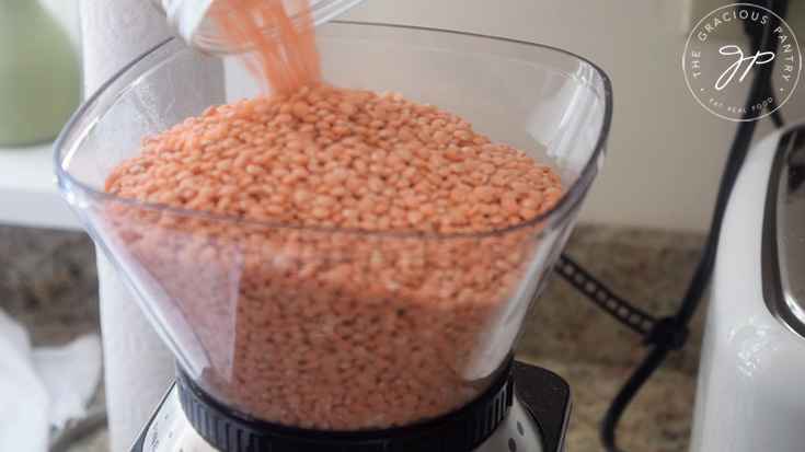 Red lentils being poured into a grinder to make flour.