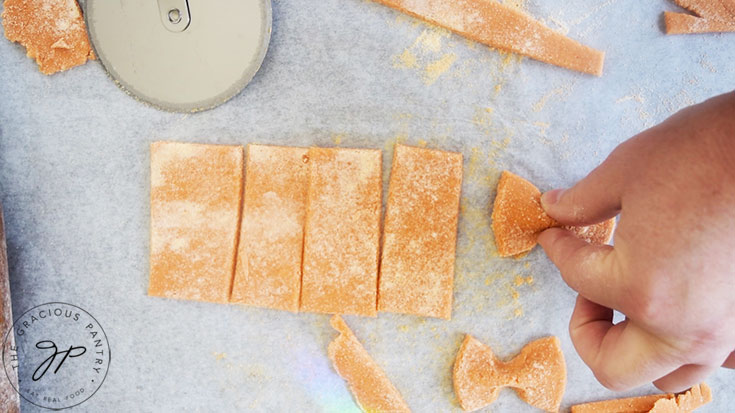 Cutting and pinching Complete Protein Pasta dough into bow tie shapes.