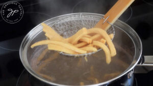 Lifting cooked pasta out of boiling water with a slotted spoon.