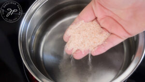 A hand adds salt to a pot of water.