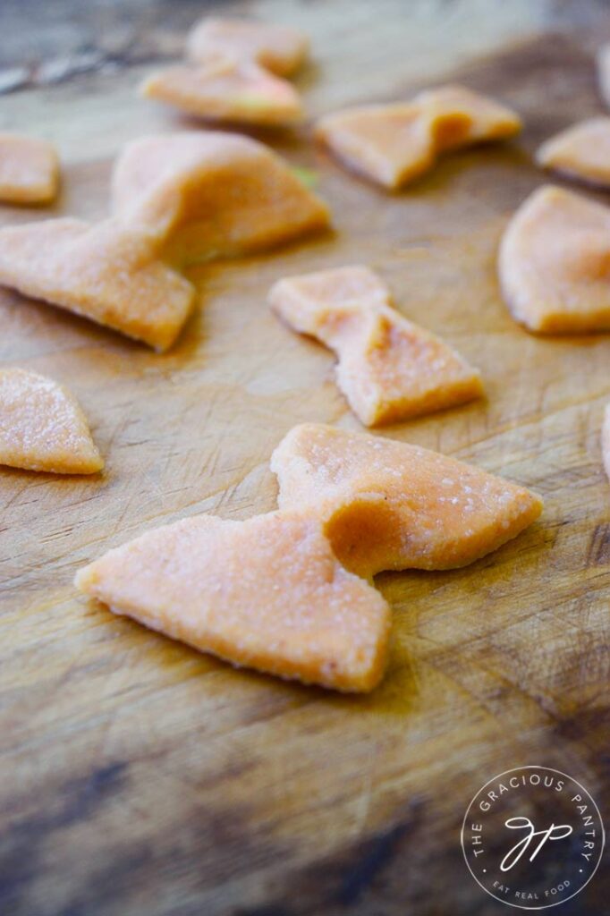 A closeup of bow tie noodles laying on a wooden surface.