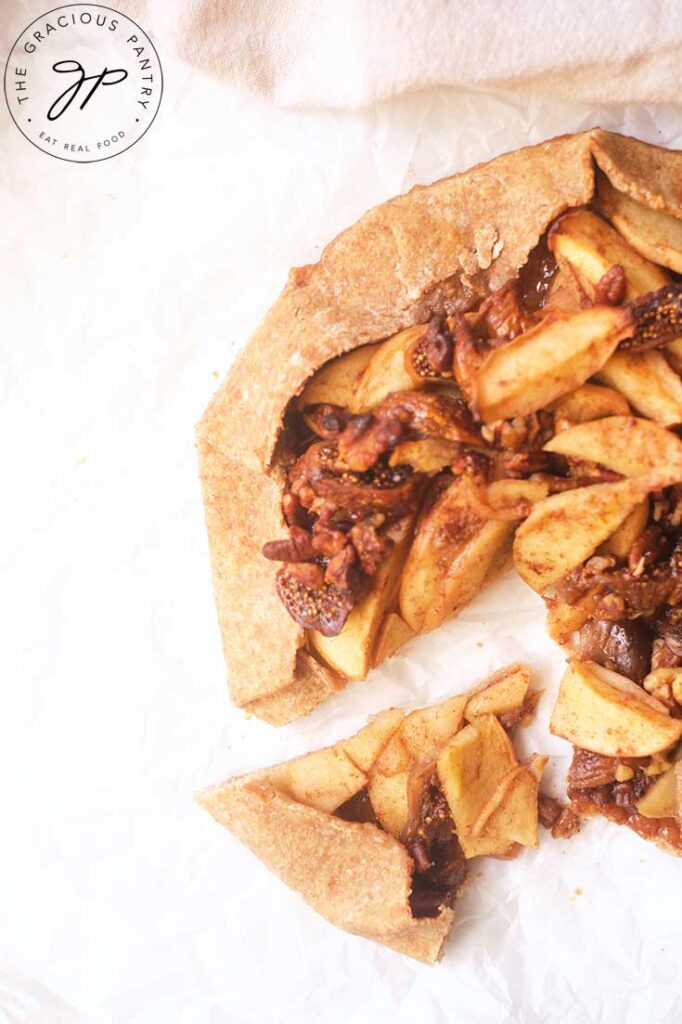 An overhead view of a Fig Galette with one piece cut and pulled back on parchment.