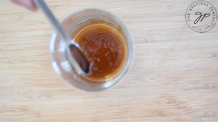 Pouring vanilla extract into a cup with maple syrup.