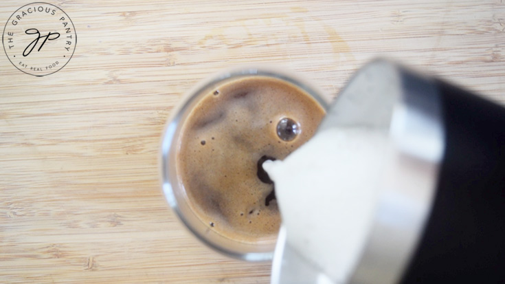 Pouring frothed milk into a cup to complete a Healthy Pumpkin Spice Latte.