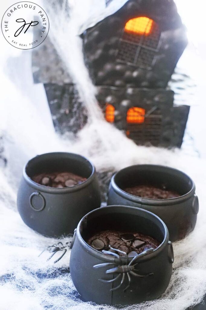 Three cauldron cakes sit in front of a black haunted house.
